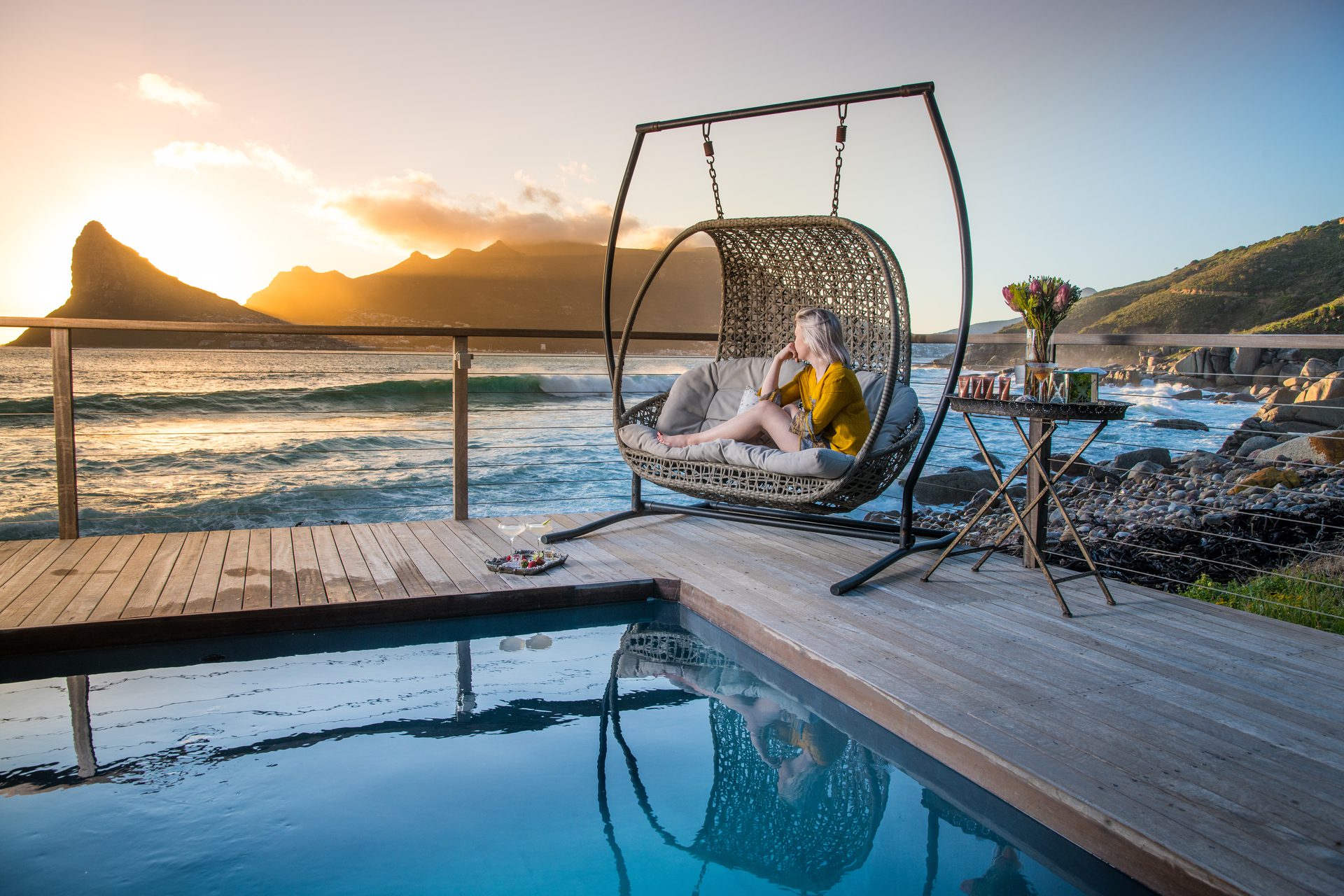 Tintswalo-Atlantic-Luxury-Boutique-Hotel-Pool-Deck-Gallery-9 A woman sits on a hanging chair overlooking the ocean and mountains at one of the luxury hotels in Cape Town
