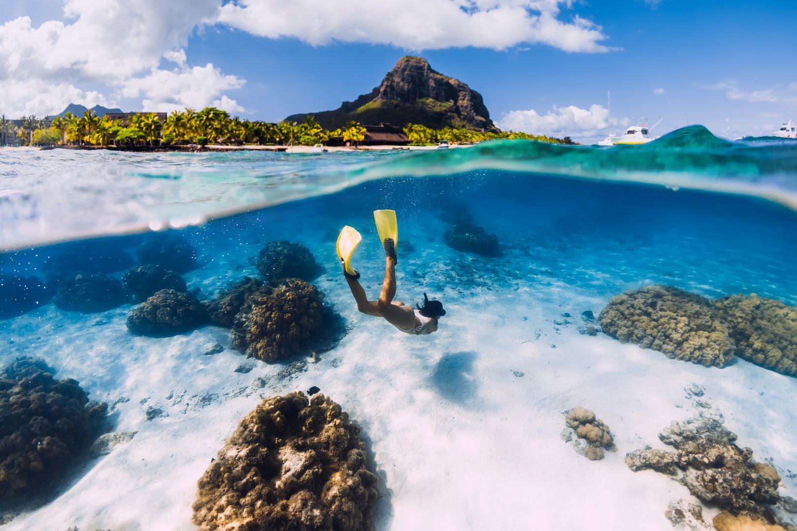 Woman freediver glides over sandy sea with yellow fins in transparent ocean. Freediving in Mauritius A snorkeller with yellow fins dives over coral reefs in clear blue waters, capturing the ocean adventures of Africa in September.